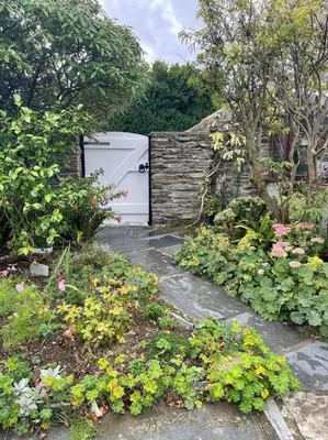 a garden with a white door and some flowers at The Hayloft - New Dog friendly with garden and parking in Port Isaac