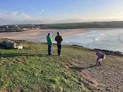 three people standing on a hill looking at the beach at 2Bed with Pool & Sea View Apartment in Newquay