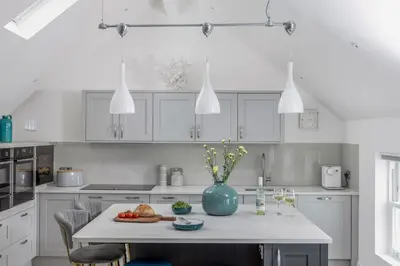 a white kitchen with a table with a blue vase on it at Loe Cottage in Helston