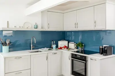 a white kitchen with blue walls and white cabinets at Loe Cottage in Helston
