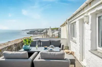 a patio with a table and chairs and the ocean at Loe Cottage in Helston