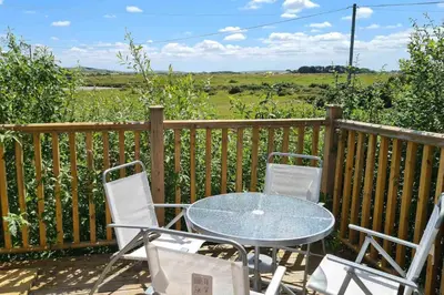 a glass table and chairs on a deck with a view at Stable Barn Apartment in Saint Breward