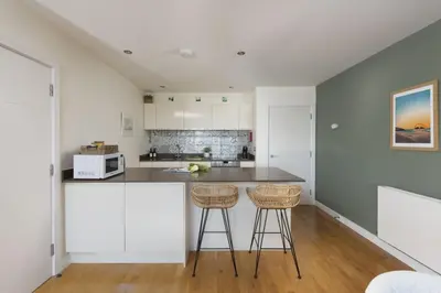 a kitchen with white cabinets and two bar stools at 6 The Point - Walk to Newquay's Beaches - Free WiFi and Parking in Newquay
