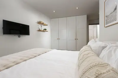 a white bedroom with a bed with a tv on the wall at 6 The Point - Walk to Newquay's Beaches - Free WiFi and Parking in Newquay