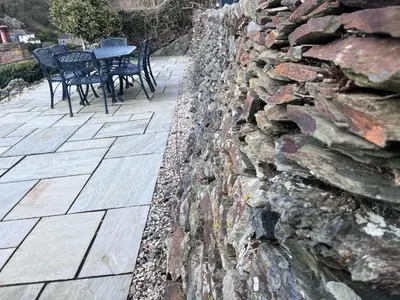 a stone wall next to a table and chairs at Cottages at the Lugger in Portloe
