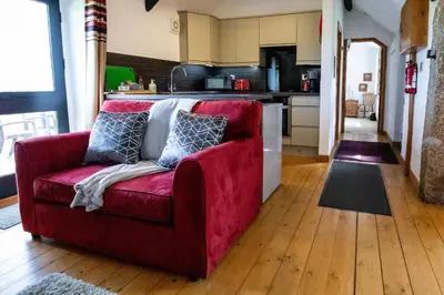 a red couch in a living room with a kitchen at Treworgie Barton - Braddon in Bude