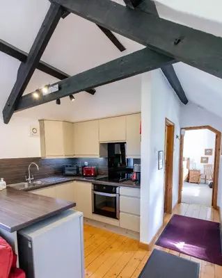 a kitchen with white cabinets and a wooden floor at Treworgie Barton - Braddon in Bude
