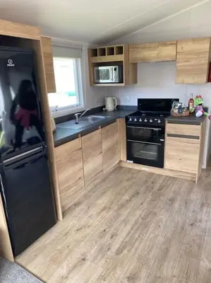 a kitchen with a black refrigerator and wooden cabinets at Cosy Caravan New for 2024! in Newquay