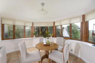 a dining room with a table and chairs and windows at Godolphin in Wadebridge