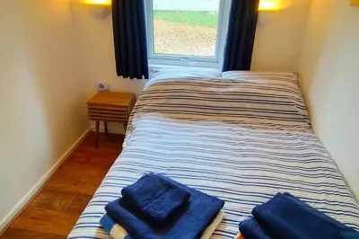a bed with blue towels on it in a room with a window at Painters Cottage 2-Bed Chalet nr St Ives & Hayle in St Ives