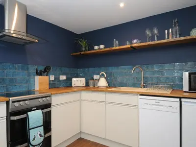 a kitchen with white cabinets and blue walls at The Bower in Helston