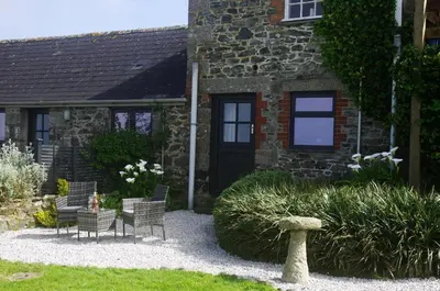 a garden with chairs and a building with a black door at The Bower in Helston