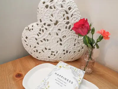 a white vase with a red rose and a plate and a vase with at Breeze Cottage in Falmouth