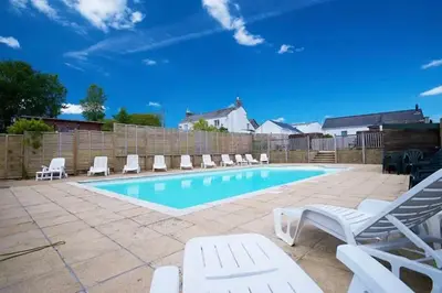 a swimming pool with lounge chairs and a fence at The Cornish hottub escape in St Austell