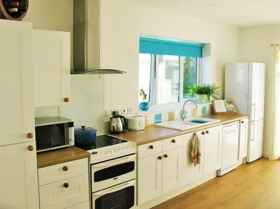 a kitchen with white cabinets and a sink and a microwave at Sunny Corner - Coastal apartment near the beach in Crantock