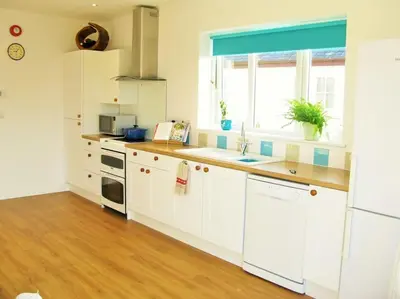 a kitchen with white cabinets and a sink and a window at Sunny Corner - Coastal apartment near the beach in Crantock