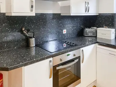 a kitchen with white cabinets and granite counter tops at Trebellan in Porthtowan