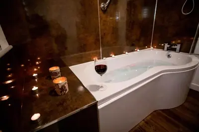 a bath tub with a glass of wine and candles at Treworgie Barton - Duchy in Bude