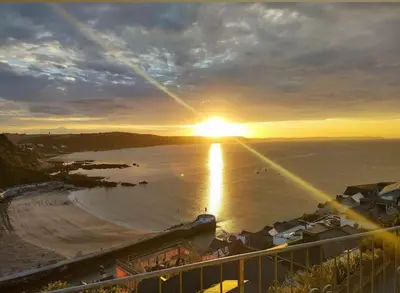 a view of a beach with the sun setting over the water at Crows Nest Apartment, at Clipper House with free onsite allocated parking in Looe