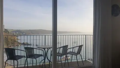 a balcony with a table and chairs and a view of the water at Crows Nest Apartment, at Clipper House with free onsite allocated parking in Looe