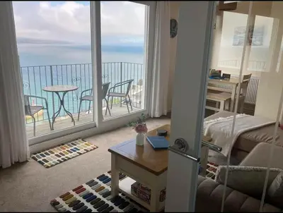 a living room with a balcony with a view of the ocean at Crows Nest Apartment, at Clipper House with free onsite allocated parking in Looe