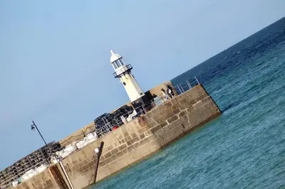 a lighthouse on a pier in the water at Sandy Feet, St Eia Street. Cosy Cottage + Parking in St Ives