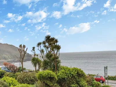 a red car parked next to the ocean with palm trees at Pegasus in Falmouth
