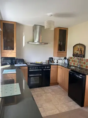 a kitchen with black appliances and wooden cabinets at Honeycomb Cottage - a quiet, charming, cosy retreat in the countryside only 2 miles from one of Cornwall's best beaches in Truro