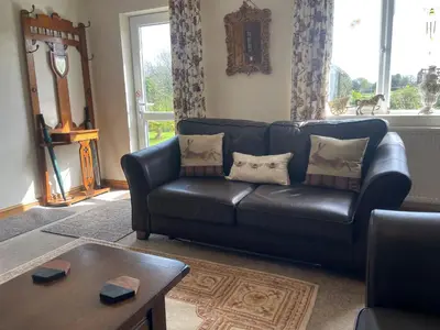 a living room with a black leather couch and a table at Honeycomb Cottage - a quiet, charming, cosy retreat in the countryside only 2 miles from one of Cornwall's best beaches in Truro