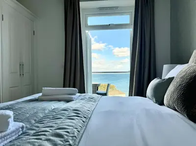 a bedroom with a bed with a view of the ocean at Luxury Sea View Apartment with Multi Room Balcony And Private Onsite Parking Only 300M From the Beach in Looe