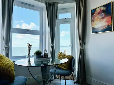 a table and chairs in a room with a window at Luxury Sea View Apartment with Multi Room Balcony And Private Onsite Parking Only 300M From the Beach in Looe