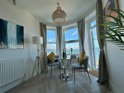 a dining room with a table and chairs and windows at Luxury Sea View Apartment with Multi Room Balcony And Private Onsite Parking Only 300M From the Beach in Looe