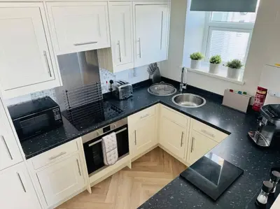a kitchen with white cabinets and a black counter top at Luxury Sea View Apartment with Multi Room Balcony And Private Onsite Parking Only 300M From the Beach in Looe