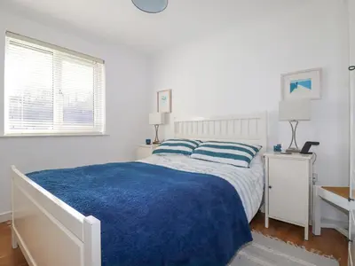 a white bedroom with a bed with a blue blanket at Carrick Cottage in Falmouth