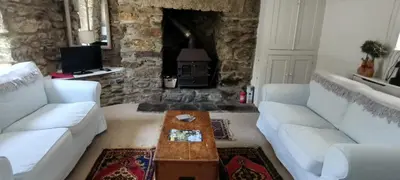 a living room with white couches and a stone fireplace at The Samphire Cottage in Porthleven