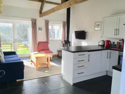 a kitchen with white cabinets and a living room at Morvoren Cottage in Launceston