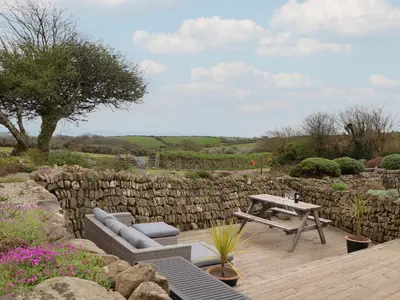 a patio with a table and benches and a stone wall at Long Barn in Penzance