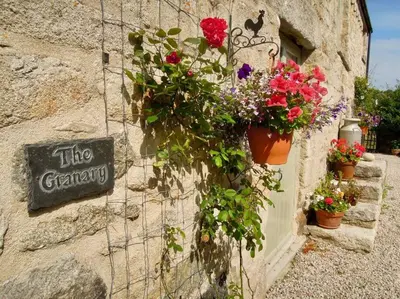 a stone wall with flowers in pots and a sign at The Granary in St Austell