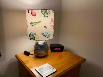 a lamp on top of a wooden table with a clock at Two Bedroomed Holiday Cottage with Sea Views in St Austell
