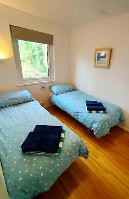 a bedroom with two beds with blue sheets and a window at Woodland View - Families & Pets in Uny Lelant
