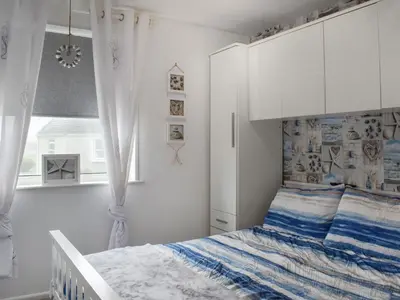a white bedroom with a bed and a window at Beach House in Perranporth