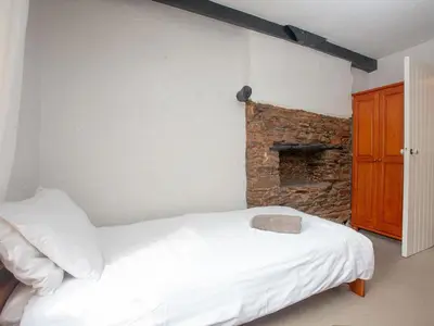a bedroom with a white bed and a brick wall at Linhay in Looe