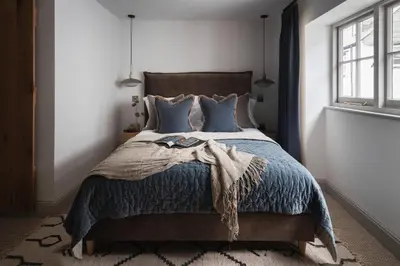 a bedroom with a bed with a blue comforter and a window at Kittiwake Cottage - Charming harbour-side cottage, luxury interiors in Port Isaac