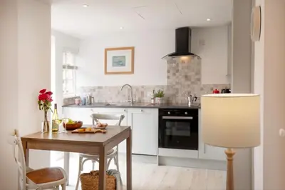 a kitchen with white cabinets and a wooden table at Lavender Cottage in Porthscatho