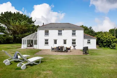 a large white house with two white chairs in the yard at Meadow House in Porthscatho