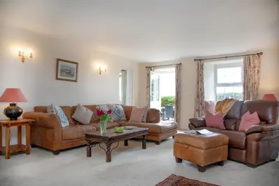 a living room with brown leather couches and a table at Meadow House in Porthscatho