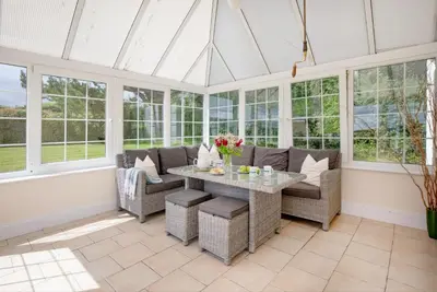 a conservatory with a table and chairs and windows at Meadow House in Porthscatho