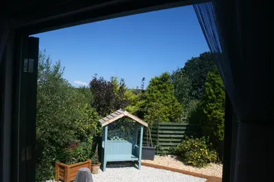 a door leading into a garden with a blue bench at TREKLYS Shepherds Hut in Otterham