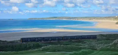 a train on tracks near a beach and the ocean at Trees Dale Lodge in Hayle in Hayle