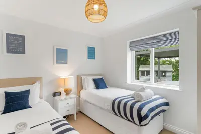 two beds in a white room with a window at The Little Hawthorns in Polzeath